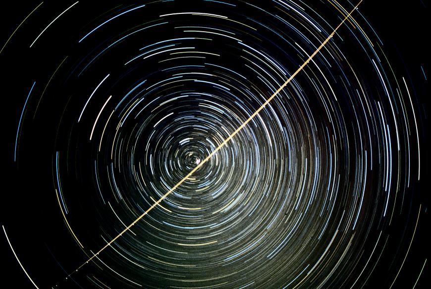 A star trail photograph showing the apparent motion of stars around the north celestial pole; Polaris is the bright star near the pole, just above the jet trail.