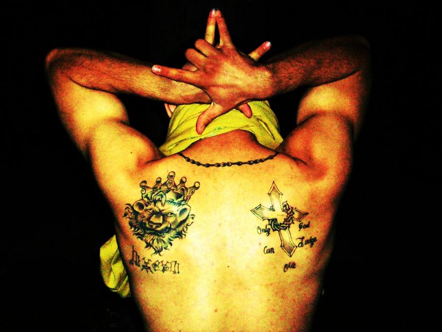 Latin King gang member showing his gang tattoos, and hand sign.