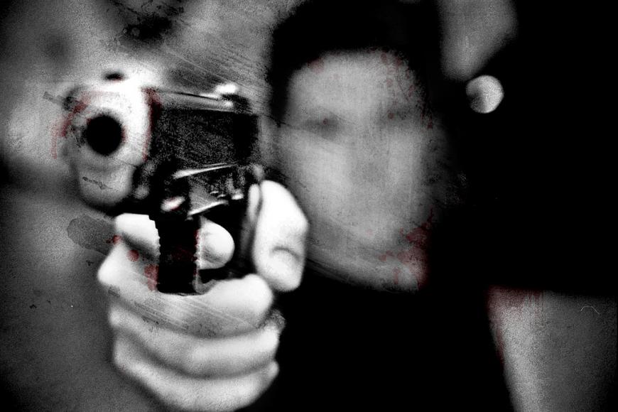 Heavily filtered black and white, blood-splattered image of a man pointing a gun at the camera.