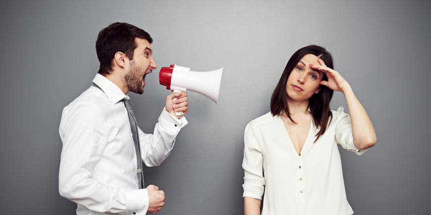 Photo of man yelling through a megaphone at an exasperated woman. Both dressed in workplace casual.