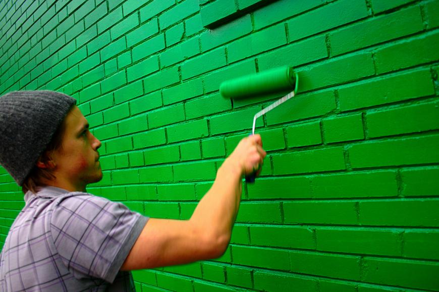 Man painting a brick wall green 