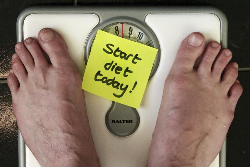 Close up of bare feet on a weigh scale with a sticky note in between reading &quot;Start Diet Today&quot;