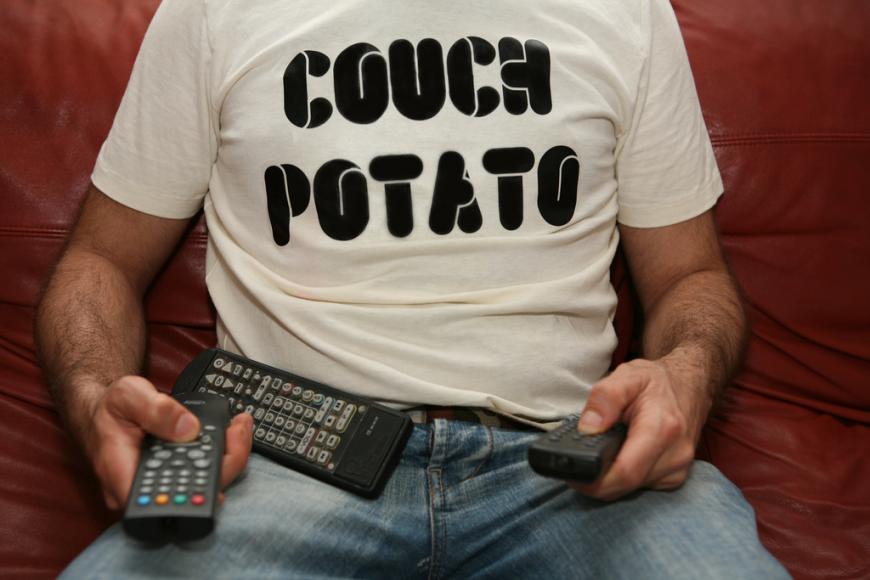 man wearing couch potato shirt with a pile of remote controls in his lap