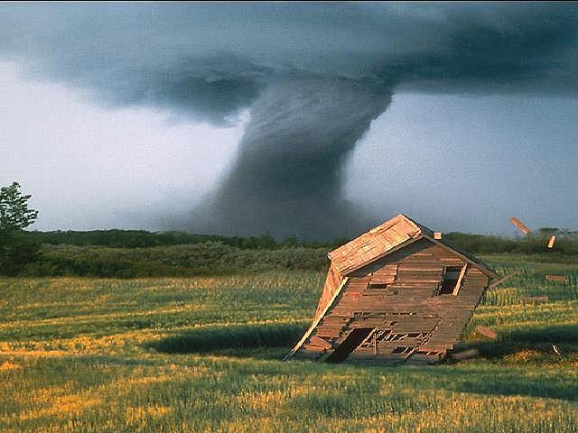 A tornado in the background. In the foreground an old wooden house tilts over in the wind.