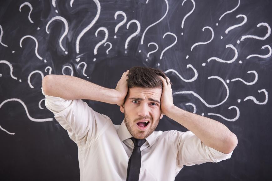 A man panicking with question marks around his head