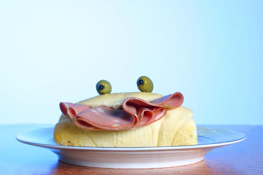 A sandwich with a mortadela smile and olive eyes.