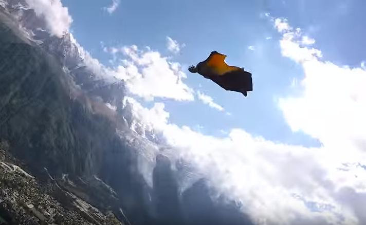 Screenshot of a wingsuit flier in the air above a small town surrounded by moutains