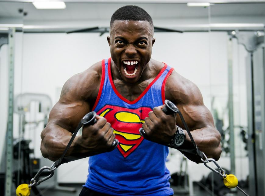 Body builder lifting weights at the gym in a Superman tanktop