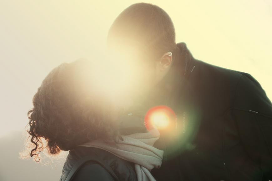 A couple kiss with a sunset directly behind them.