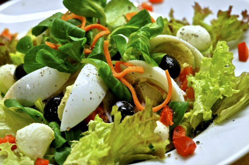 a salad with lettuce, hard boiled eggs, olives, and red bell pepper