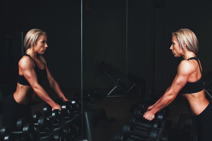Woman lifting weights off the rack, looks at herself in the mirror