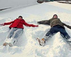 Man and woman making snow angels in the snow.