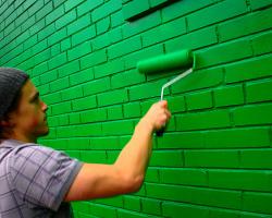Man painting a brick wall green 