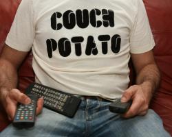 man wearing couch potato shirt with a pile of remote controls in his lap