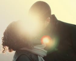 A couple kiss with a sunset directly behind them.