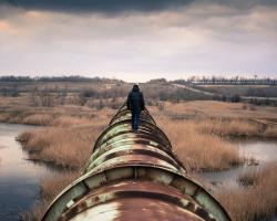 Man walking along the top of a rusty pipeline
